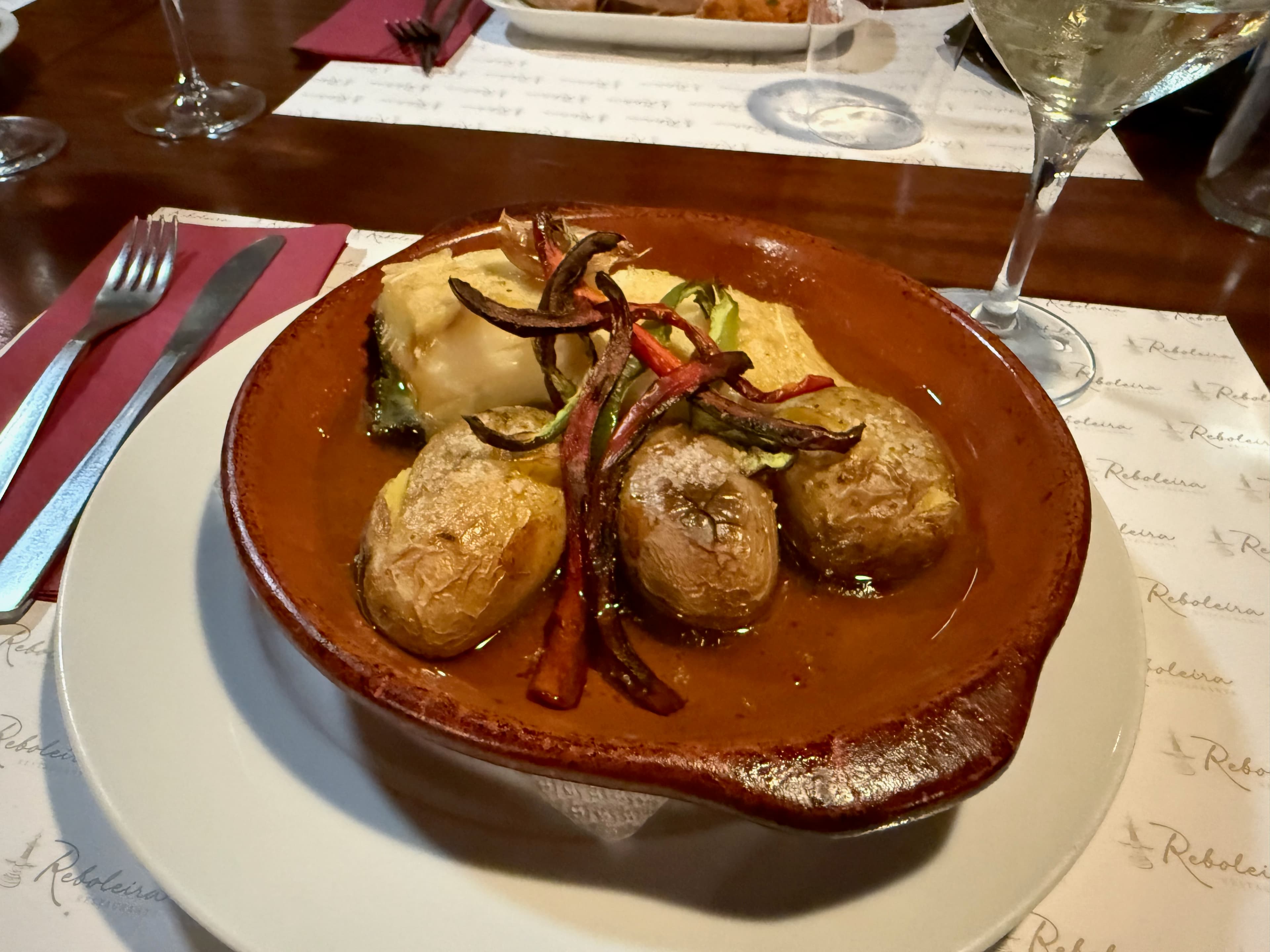 A close-up of the perfectly cooked cod fish with roasted potatoes swimming in golden olive oil.